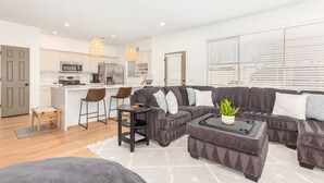 A modern living room with a grey sectional sofa, a coffee table, and a small dining area with bar stools. - Resort-like 2BR/2BA townhome in sunny Scottsdale near golf, hike, dine, shop etc (Scottsdale)