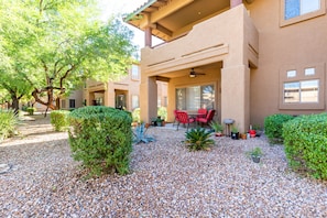 A building with a covered patio area, red chairs, and potted plants.