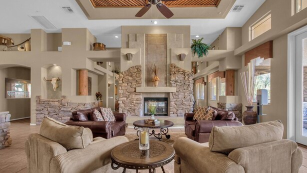 A spacious living room with a stone fireplace, leather sofas, and a ceiling fan. - Resort-like 2BR/2BA townhome in sunny Scottsdale near golf, hike, dine, shop etc (Scottsdale)