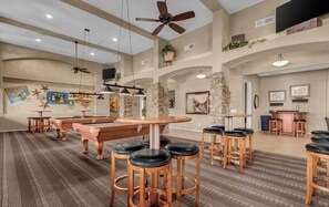 A spacious indoor area with a pool table, bar stools, and a ceiling fan.