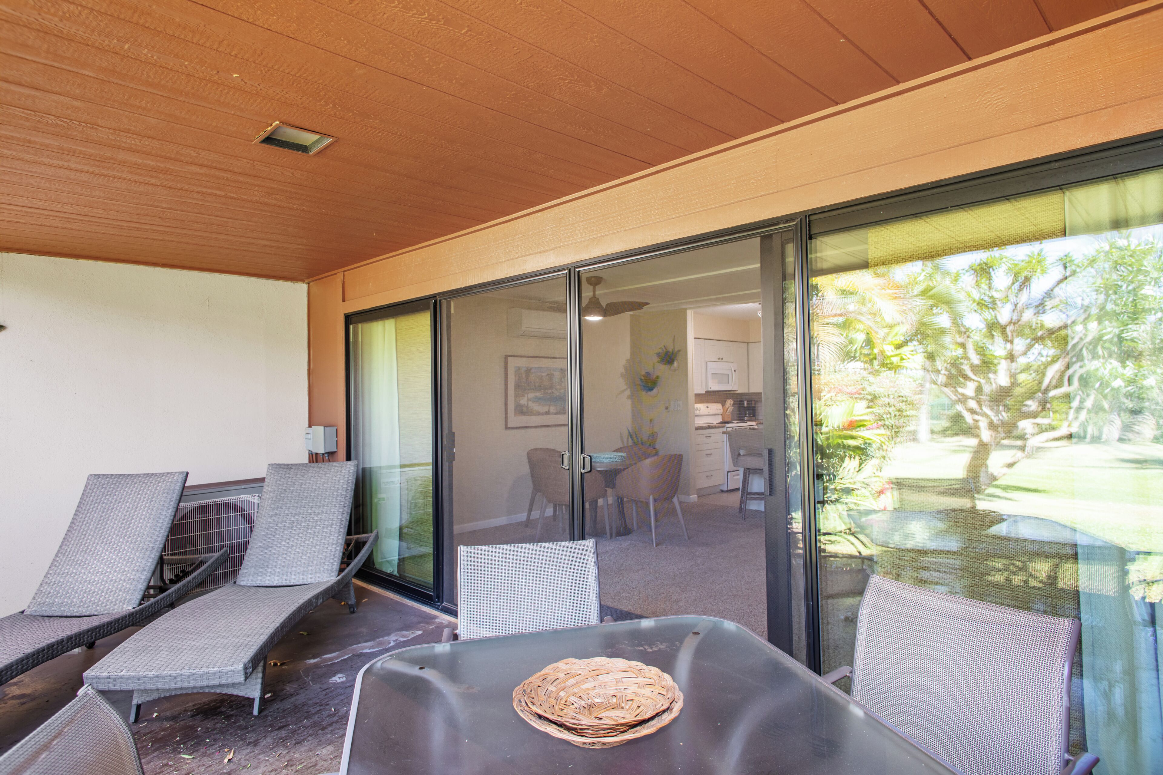 A covered outdoor seating area with chairs and a table, a view of the backyard through glass doors, and a ceiling with recessed lighting.