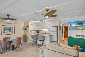 A modern kitchen with white cabinets, a central island, and a dining area with chairs and a table.