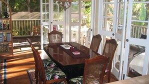 A covered dining area with a wooden table and chairs, surrounded by glass doors and windows.