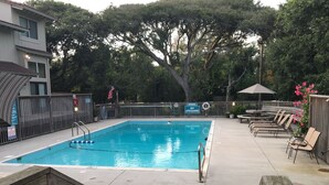 A swimming pool with a wooden deck, lounge chairs, and a lifeguard sign.