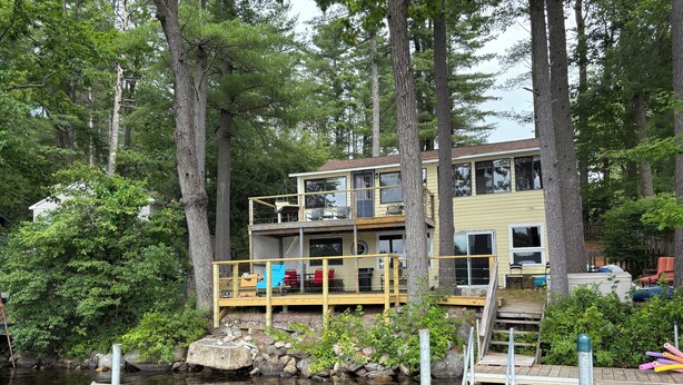 A multi-level house with a dock extending into a calm body of water, surrounded by tall trees. - Peaceful Lakefront 3 bedroom Cottage On Quiet Forest Lake  (Gray)