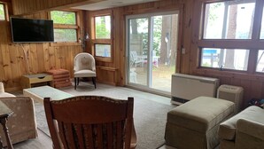 A wooden-paneled room with a television, a chair, a small table, and a sliding glass door leading to an outdoor area. - Peaceful Lakefront 3 bedroom Cottage On Quiet Forest Lake  (Gray)