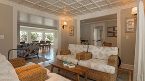 A spacious living room with a large sofa, a coffee table, and wicker chairs. There are framed pictures on the walls and a window with a view of the outdoors. - Rehoboth Beach Lake Front Private Pool Home Sleeps 12 (Rehoboth Beach)