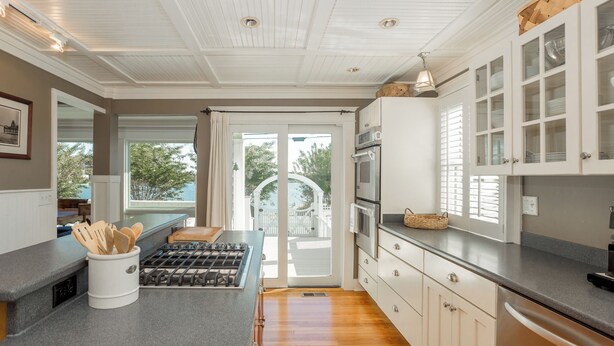 A modern kitchen with white cabinetry, a gas stove, and a view through the glass doors to the outdoors. - Rehoboth Beach Lake Front Private Pool Home Sleeps 12 (Rehoboth Beach)