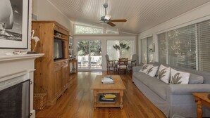 A spacious living room with a fireplace, a ceiling fan, and a large window with blinds. - Rehoboth Beach Lake Front Private Pool Home Sleeps 12 (Rehoboth Beach)
