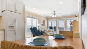 A dining area with a wooden table, blue bowls, wicker chairs, a white refrigerator, and a blue chair in the background.