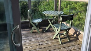 A wooden deck with a glass door, two green chairs, and a small table. - Single level home, near beach. Ultra clean. Great location -Walk to everything! (Yachats)