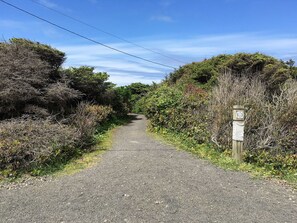 A gravel path flanked by dense vegetation and a wooden post with a sign. - Single level home, near beach. Ultra clean. Great location -Walk to everything! (Yachats)
