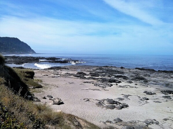 A rocky beach with waves crashing against the shore, a clear sky, and a distant mountain. - Single level home, near beach. Ultra clean. Great location -Walk to everything! (Yachats)