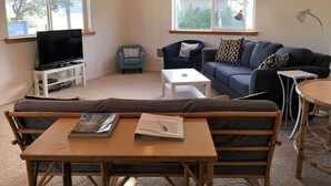 A living room with a TV, two sofas, a coffee table, and a small table with magazines. - Single level home, near beach. Ultra clean. Great location -Walk to everything! (Yachats)