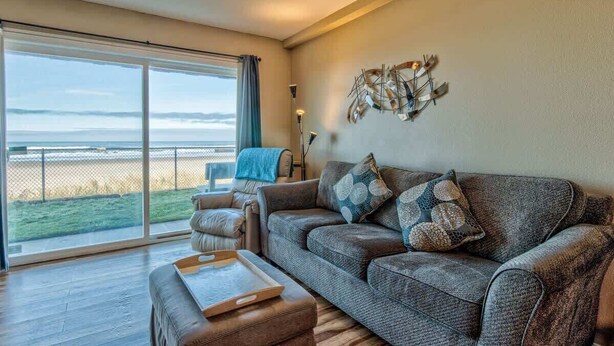 A spacious living room with a large sliding glass door leading to a balcony overlooking a beach.