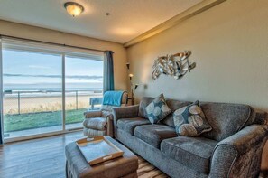 Een ruime woonkamer met een grote schuifpui naar een balkon met uitzicht op een strand.