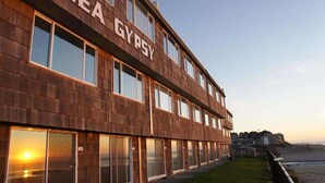 A multi-story building with the name "SEA GYPSY" on the facade, large windows, and a view of the beach.
