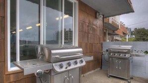 An outdoor kitchen area with a stainless steel grill and a built-in oven, adjacent to a wooden house with large windows.