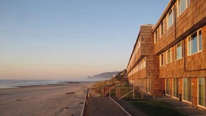 A beachfront hotel with a long, straight pathway leading to the beach, wooden exterior, and large windows.