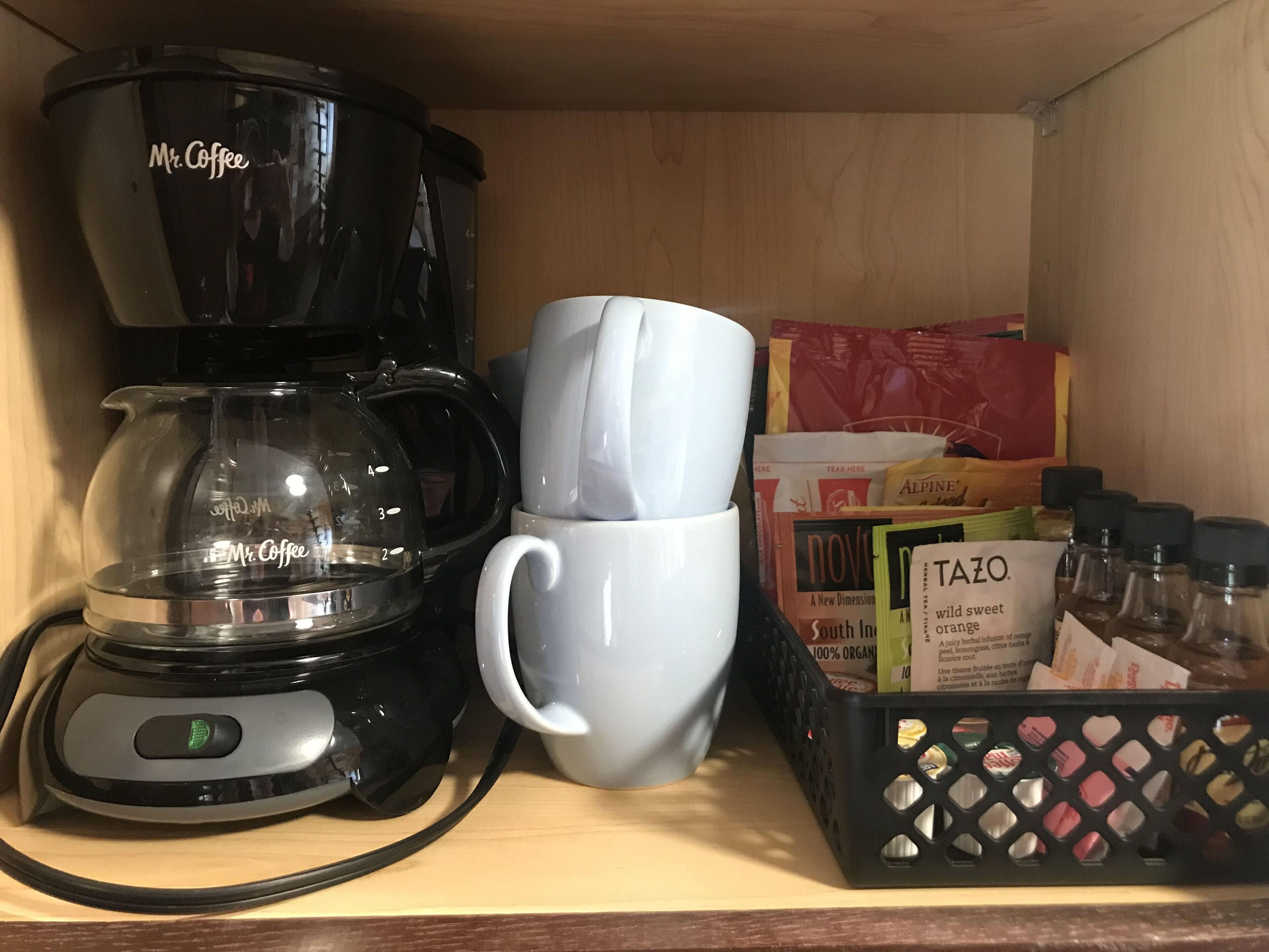 A coffee maker, a mug, and a box of Tazo tea bags on a shelf.