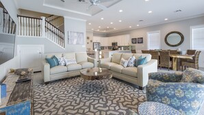 Ein geräumiges Wohnzimmer mit hohen Decken, einem zentral platzierten Couchtisch und einer Treppe, die zu einer oberen Ebene führt.