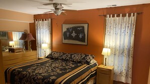 Un dormitorio con una cama grande, un ventilador de techo, un aparador, una mesita de noche y un cuadro en la pared.