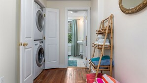 Un cuarto de lavado con lavadora, un tendedero con toallas de colores y un espejo en la pared.