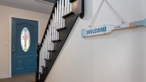 Una escalera con un cartel de 'WELCOME', una puerta azul con un vitral y una pared blanca.