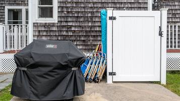 Een overdekte grill met een Weber logo, een witte garage deur, en een blauwe zeildoek tegen de deur geleund.