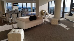 A spacious lobby with a white sofa, ottoman, and a small round table with glasses. Large windows offer a view of the ocean. -   Surfside Resort , Great Views, Huge Balcony (Destin)