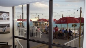 A view from inside a room with large windows overlooking a deck area with outdoor seating, umbrellas, and a view of the sea. -   Surfside Resort , Great Views, Huge Balcony (Destin)