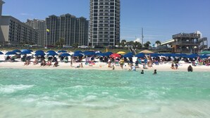 A beach with clear turquoise water, numerous umbrellas, and people enjoying the sand. -   Surfside Resort , Great Views, Huge Balcony (Destin)