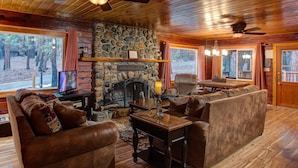 Un interior de cabaña acogedor, con chimenea de piedra, mobiliario de cuero y televisor.