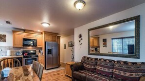 A compact kitchen with wooden cabinets, a microwave, and a refrigerator. There is a dining table with chairs and a sofa with patterned cushions. A large mirror hangs on the wall. - Inside Yosemite Park-Yosemite Spring Wonderland (Yosemite National Park)