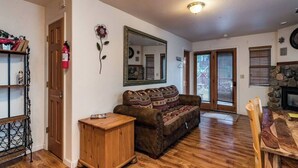 A living room with a wooden floor, a sofa, a coffee table, a fireplace, and a door leading to another room. - Inside Yosemite Park-Yosemite Spring Wonderland (Yosemite National Park)