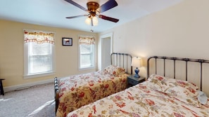 A bedroom with two beds, a ceiling fan, and a nightstand with a lamp.