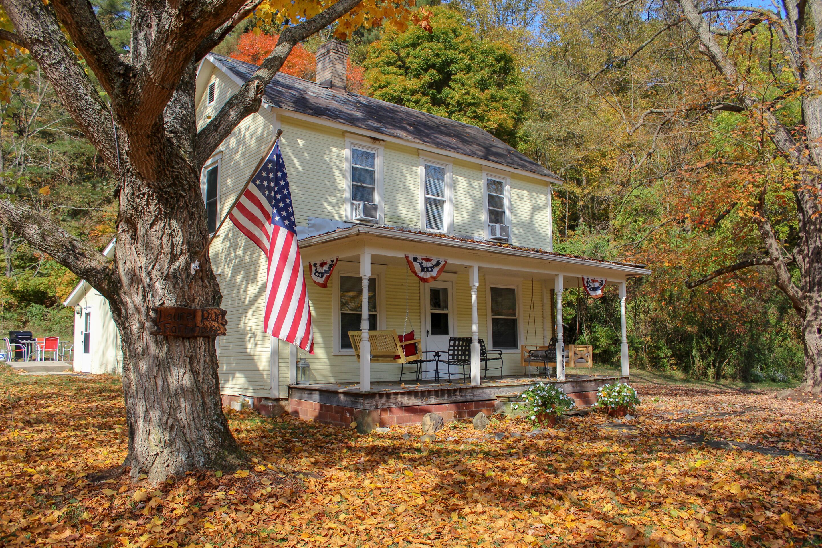 Ein zweistöckiges Haus mit Veranda, einer amerikanischen Flagge und einem Schild mit der Aufschrift 'Laurel Pub Farmhouse'.