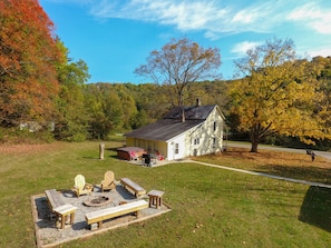 A rustic cabin with a fire pit and outdoor seating, surrounded by autumn foliage and a clear sky.