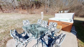 An outdoor patio with a glass table surrounded by patterned chairs, a wooden hot tub, and a concrete floor.