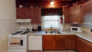 A kitchen with wooden cabinets, a gas stove, a dishwasher, a microwave, and a window with blinds.