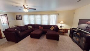 A living room with a sectional sofa, a ceiling fan, a television, and a small table with a lamp. - Lovely Laurel Run Cottage, Hocking Hills, Hot Tub (Nelsonville)