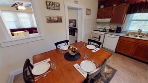 A dining area with a wooden table set for four, a ceiling fan, and a kitchen with wooden cabinets and a stove.