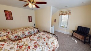 A bedroom with two beds, a ceiling fan, a window with a curtain, and a television on a stand.