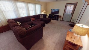 A living room with a sectional sofa, a TV, a lamp, and a door. - Lovely Laurel Run Cottage, Hocking Hills, Hot Tub (Nelsonville)