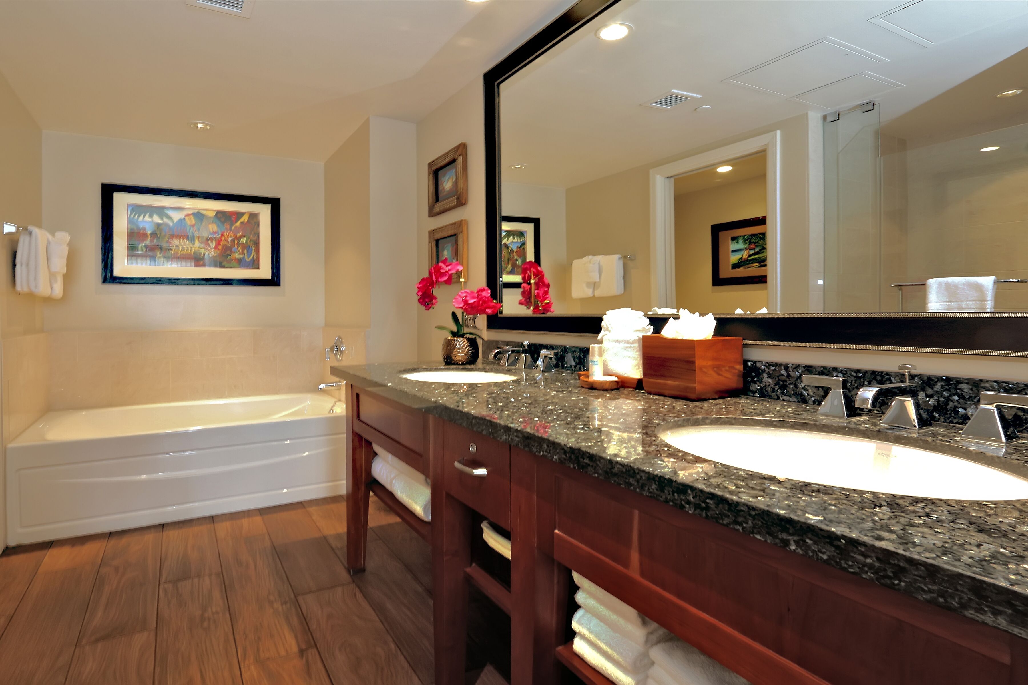 A modern bathroom with a bathtub, two sinks, a large mirror, and wooden cabinets.