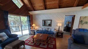Un salon chaleureux avec un plafond en bois, un canapé bleu, une table basse en bois et une grande fenêtre avec des rideaux.