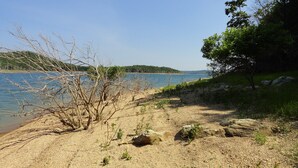 Une plage au rivage sablonneux, avec une végétation clairsemée, et une étendue d’eau calme en arrière-plan.