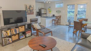 Ein Wohnzimmer mit Fernseher, Bücherregalen, einem Couchtisch und einem Essbereich mit Stühlen und Tisch.