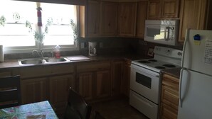 Una cocina con gabinetes de madera, un lavamanos, una cafetera, un microondas y un refrigerador.