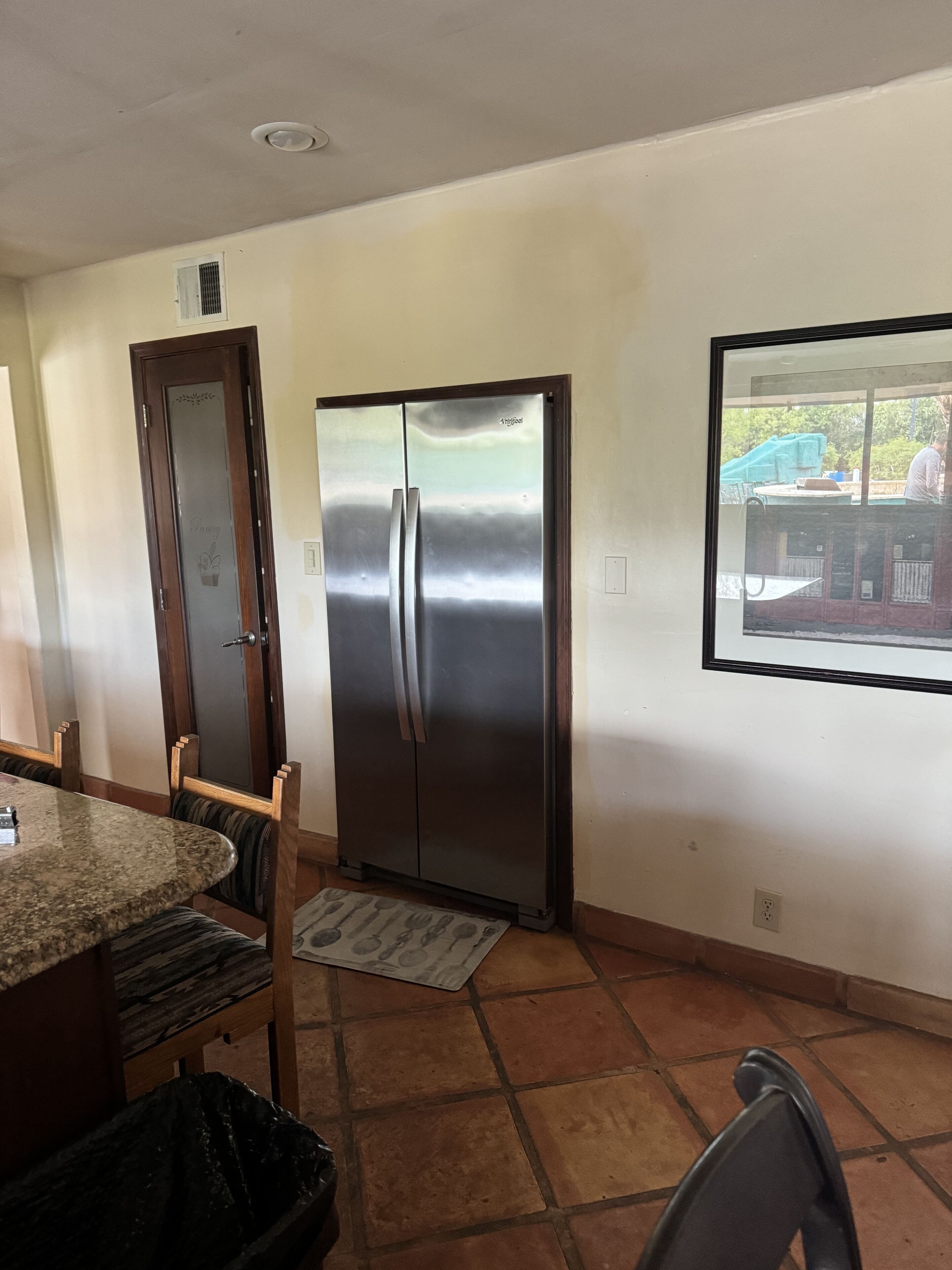 A kitchen with a stainless steel refrigerator, a dining table with chairs, and a window with a view of a playground.